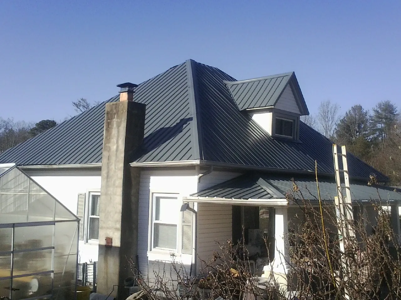 Dark blue standing seam metal roof on a white farmhouse with dormer — Slate & Tile Roof Repair by Roofing Brothers in Mastic