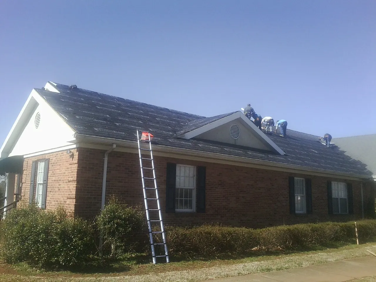 Crew tearing shingles off a brick ranch roof with a ladder set — Metal Roof Repair work by our crew in Mastic