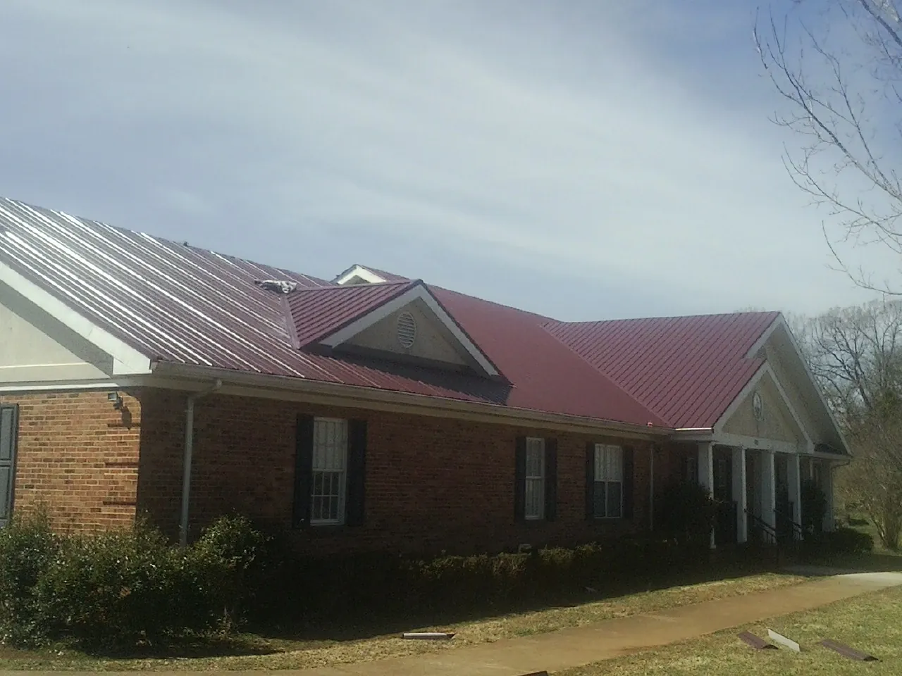 Red metal roof with gabled entries on a long brick building, from a Hail Damage Roof Repair job in Mastic