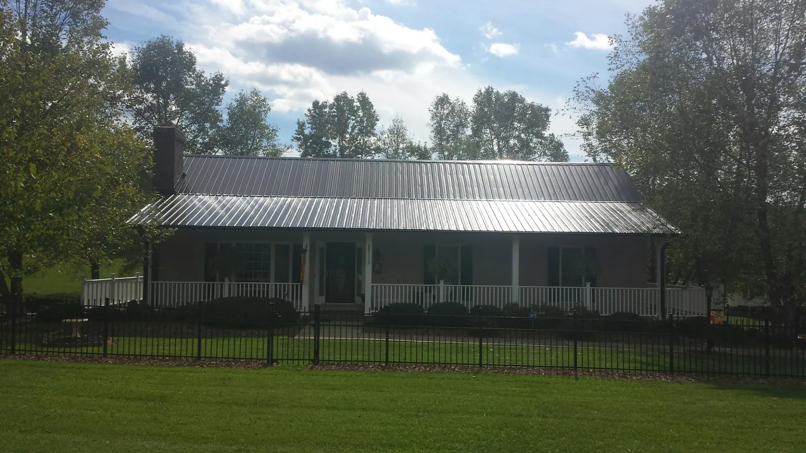 Gray metal roof on a brick ranch with a full width front porch — Gutter Guard Installation work by our crew in Mastic