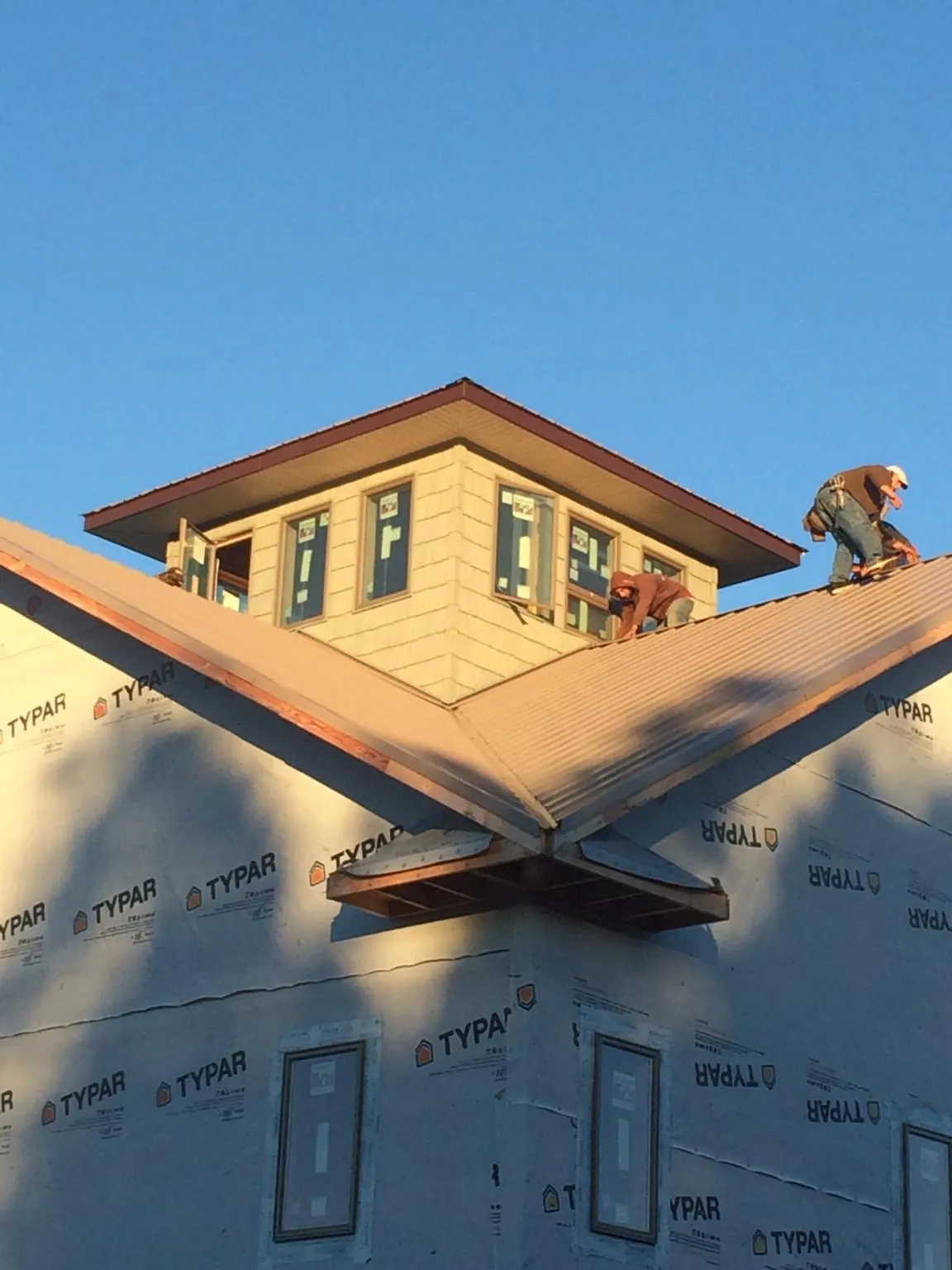 Roofers working around a rooftop cupola on a new metal roof at sunset — Roof Waterproofing in Mastic by Roofing Brothers